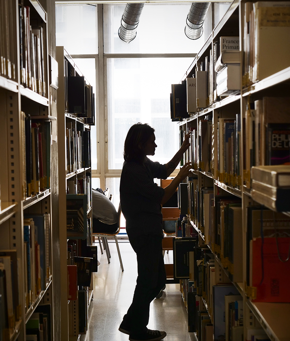 Mujer cogiendo libros en una de las estanterías de la biblioteca en la Facultad de Filosofía y Letras